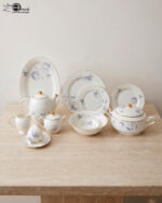 A complete super bone china dinner set in file 3.jpg featuring a delicate blue rose pattern, gold-rimmed edges, and including a teapot, plates, bowls, and serving dishes on a marble surface.