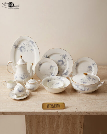 An elegant, white super bone dinner set with a delicate blue rose floral pattern and gold rims, displayed on a beige marble tabletop against a neutral background. The set includes dinner plates, side plates, a large oval serving platter, a covered casserole dish, a teapot, a sugar bowl, a creamer pitcher, a teacup with a saucer, and serving bowls