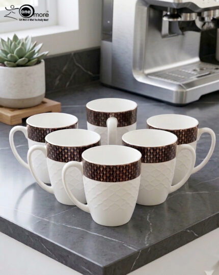 A high-angle shot of a premium white bone china mug with a textured diamond pattern and a dark geometric border, filled with latte art on a wooden table alongside a leather journal and coffee beans