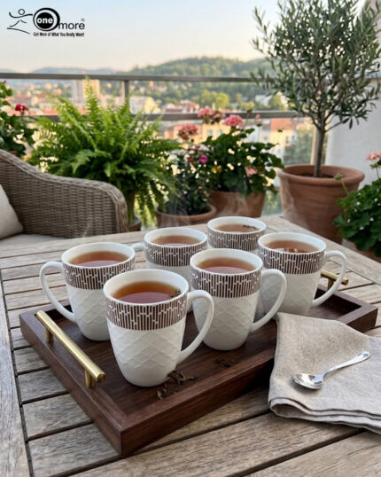 A steaming cup of green tea in a white bone china mug with a bronze geometric pattern and embossed lattice texture, sitting on a wooden table