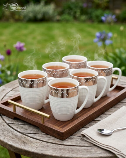 A high-angle shot of a white bone china mug filled with tea, featuring a gold geometric pattern on a wooden outdoor table with a gold spoon and green garden background