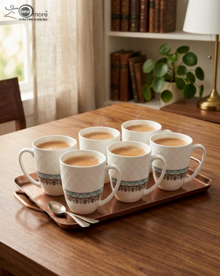 A set of white bone china mugs featuring a diamond-embossed top half and a decorative gold and teal traditional pattern at the bottom, filled with steaming tea on a wooden desk