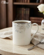 A high-angle shot labeled 3.jpg showing two elegant white bone china mugs with floral patterns and silver rims on a marble countertop next to silver spoons