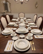 Luxury Super Bone China dinnerware set featuring a delicate white floral pattern, gold-rimmed edges, and matching tea service pieces on a wooden surface