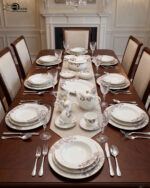 A luxury super bone china dinnerware set featuring a white base with intricate purple leaf patterns and gold accents, displayed on a wooden table