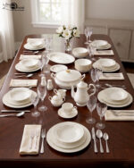 An elegant white super bone china dinner set featuring delicate beige floral patterns and gold rims, arranged on a textured beige surface. The set includes plates, bowls, a teapot, a covered casserole dish, a cream pitcher, a sugar bowl, and a teacup with a saucer.