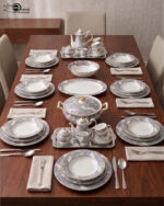 A luxury grey and white floral pattern bone china tea set and plates arranged on a wooden table, including a teapot, teacup with saucer, creamer, sugar bowl, and dinner plates.