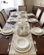 An elegant white super bone china dinner set with gold rims and a delicate grey leaf pattern, displayed on a wooden table