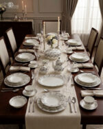 An elegant white and grey floral patterned super bone china dinner set arranged on a wooden table, including plates, bowls, a teapot, a casserole dish, and teacups.