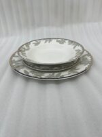 Stacked 18-piece super bone china plate set with elegant green floral patterns and gold rims on a wooden dining table setting.