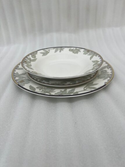 Stacked 18-piece super bone china plate set with elegant green floral patterns and gold rims on a wooden dining table setting.