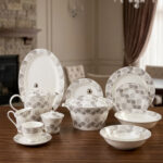 Elegant 61-piece white Super Bone China dinner set with grey floral patterns, including plates, bowls, a teapot, and a lidded casserole dish, displayed on a wooden table.