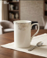 A high-angle shot labeled 3.jpg showing two elegant white bone china mugs with floral patterns and silver rims on a marble countertop next to silver spoons