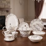 Elegant 61-piece white Super Bone China dinner set with grey floral patterns, including plates, bowls, a teapot, and a lidded casserole dish, displayed on a wooden table.