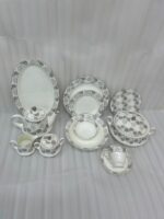 A complete Super Bone China dinner set from 6.jpg, featuring a white base with intricate grey floral borders. The set includes plates, bowls, a teapot, a tureen, and teacups displayed on a wooden surface
