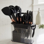 A comprehensive 17-piece kitchen tool set featuring black and rose gold silicone utensils, a matching knife set with marble-patterned handles, a vegetable peeler, kitchen shears, and a black cutting board, all stored in a clear geometric textured organizer.