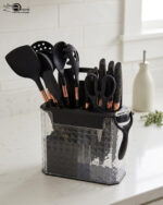 A comprehensive 17-piece kitchen tool set featuring black and rose gold silicone utensils, a matching knife set with marble-patterned handles, a vegetable peeler, kitchen shears, and a black cutting board, all stored in a clear geometric textured organizer.