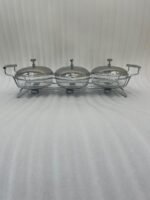 A Paramount Series 3-in-1 stainless steel food warmer buffet server with three 1.5L glass dishes and polished metal lids, featuring integrated buffet burner holders on a set dining table.