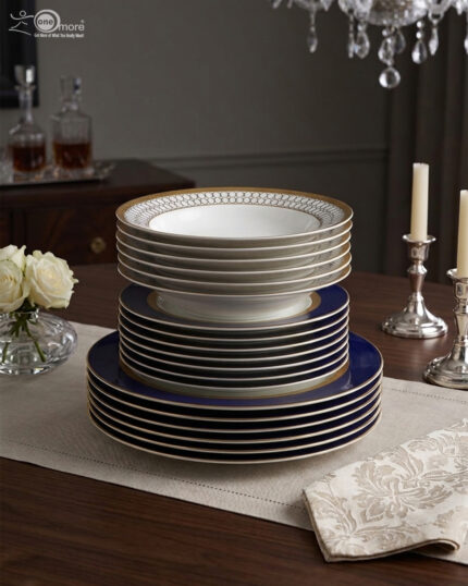 A stacked 18-piece premium super bone china dinnerware set featuring royal blue, gold rims, and geometric patterned borders, elegantly arranged on a wooden dining table with candles and roses.