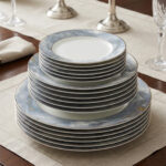 A neatly stacked 18-piece luxury super bone china plate set on a dining table runner. The dinnerware features a contemporary blue and gray ocean marble pattern with subtle gold vein accents and a thin silver rim. The stack consists of three sizes: small quarter plates on top, medium deep soup plates in the middle, and large flat rice plates at the bottom, displayed in a brightly lit, elegant dining room setting with candlesticks in the background.