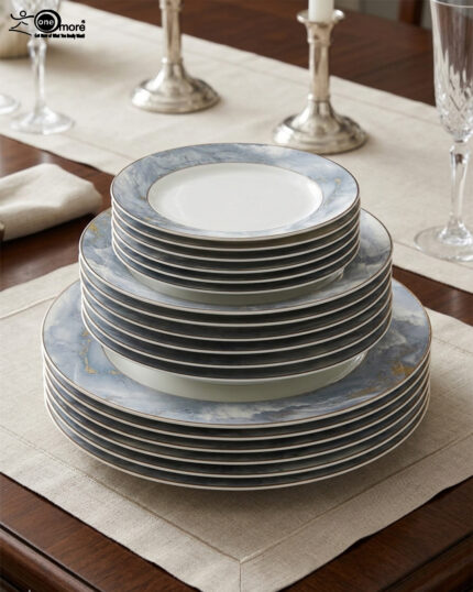 A neatly stacked 18-piece luxury super bone china plate set on a dining table runner. The dinnerware features a contemporary blue and gray ocean marble pattern with subtle gold vein accents and a thin silver rim. The stack consists of three sizes: small quarter plates on top, medium deep soup plates in the middle, and large flat rice plates at the bottom, displayed in a brightly lit, elegant dining room setting with candlesticks in the background.