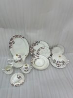 A luxury super bone china dinner set featuring a white base and intricate brown acanthus leaf patterns, including plates, bowls, a teapot, and serving dishes on a wooden table.