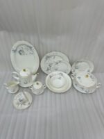 An elegant collection of super bone china dinnerware from the file 7.jpg, featuring a delicate blue rose pattern and gold-rimmed edges. The set includes a large oval platter, various sized plates, a lidded tureen, a teapot, a creamer, a sugar bowl, and a teacup with a saucer, all arranged on a light marble surface against a neutral background.