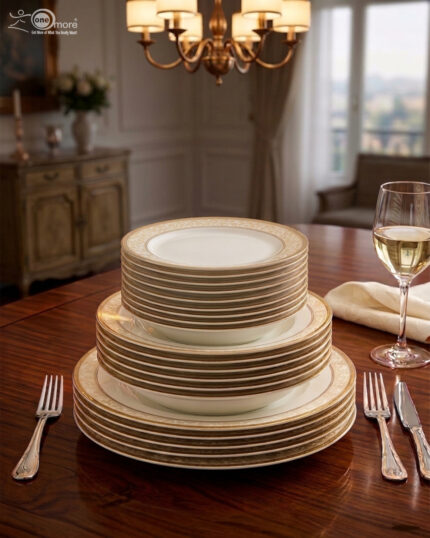 A stacked 18-piece white Super Bone China dinner plate set with elegant gold borders, arranged neatly on a polished wooden dining table alongside a wine glass and silverware under warm chandelier lighting.