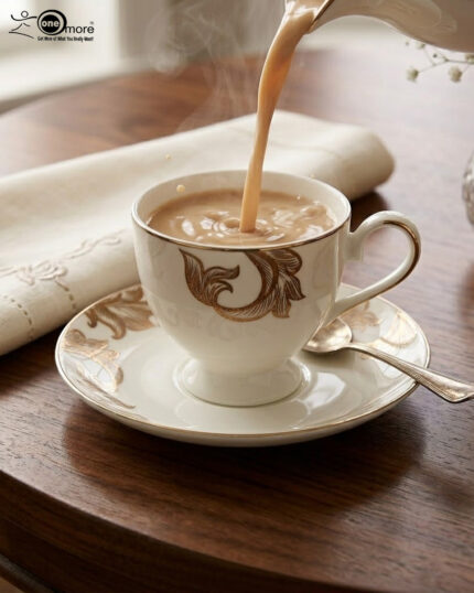 A steaming stream of milk tea being poured into a luxury white Super Bone China cup with gold-leaf designs, resting on a matching saucer with a silver spoon on a dark wooden table