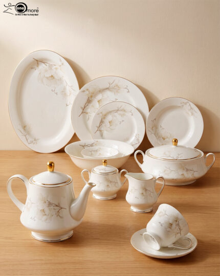 A complete super bone china dinnerware set in 7.jpg, featuring white plates, bowls, a teapot, and tea cups adorned with delicate cream floral patterns and luxurious gold-rimmed edges on a wooden surface.
