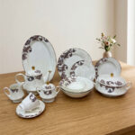 A luxury super bone china dinner set featuring a white base and intricate brown acanthus leaf patterns, including plates, bowls, a teapot, and serving dishes on a wooden table.