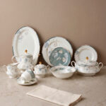 A luxury super bone china dinner set with delicate blue floral patterns and gold accents, including plates, bowls, and a tea service set on a marble surface.