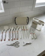 A comprehensive 16-piece kitchen tool set featuring cream-colored silicone utensils with marble-patterned handles, rose gold accents, a matching knife set, kitchen shears, a peeler, and a cutting board, all stored in a clear geometric organizer.