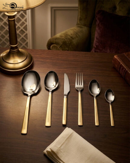 A 36-piece luxury One More cutlery set featuring elegant gold-accented handles with a geometric Greek key pattern, arranged professionally on a dark wood dining table.