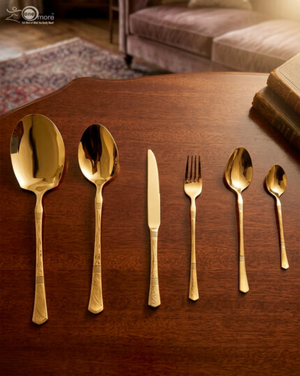 High-angle studio shot of a 36-piece gold-plated cutlery set arranged on a polished wooden surface, featuring matching serving pieces, dinner spoons, forks, knives, and teaspoons with elegant handle detailing.