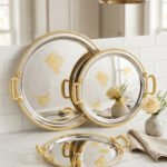 A luxury 3-piece round stainless steel serving tray set with gold textured handles and etched gold floral designs, arranged on a marble kitchen countertop as shown in 1.jpg.