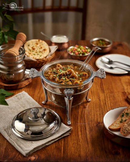 One More 4-liter glass chafing dish soup warmer with ornate stainless steel stand, ladle, and buffet burner on a wooden dining table.