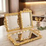 An elegant rectangular stainless steel serving tray with a highly reflective mirror finish and intricate center engravings, featuring a luxurious ornate gold border and decorative handles, displayed on a dark wooden table as shown in 1.jpg.