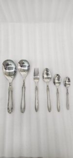 A fork and spoon from the 37-piece stainless steel cutlery set elegantly placed on a linen napkin next to a freshly served pasta dish.