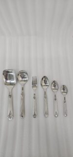 A complete 37-piece stainless steel cutlery set, including various spoons, forks, and knives with decorative handles, displayed on a linen tablecloth as shown in 7.jpg.
