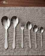 A fork and spoon from the 37-piece stainless steel cutlery set elegantly placed on a linen napkin next to a freshly served pasta dish.