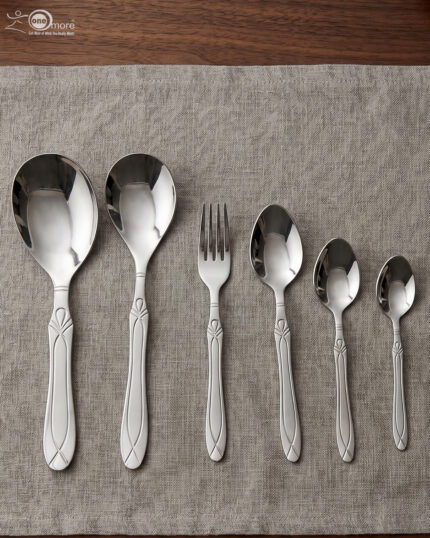 A fork and spoon from the 37-piece stainless steel cutlery set elegantly placed on a linen napkin next to a freshly served pasta dish.