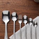 Overhead view of a 37-piece stainless steel cutlery set, including table spoons, forks, knives, and serving utensils arranged on a wooden table, as depicted in 7.jpg.