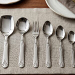 A complete 37-piece stainless steel cutlery set, including various spoons, forks, and knives with decorative handles, displayed on a linen tablecloth as shown in 7.jpg.