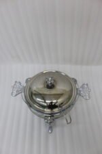 One More 4-liter glass chafing dish soup warmer with ornate stainless steel stand, ladle, and buffet burner on a wooden dining table.