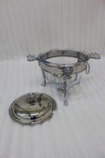 One More 4-liter glass chafing dish soup warmer with ornate stainless steel stand, ladle, and buffet burner on a wooden dining table.