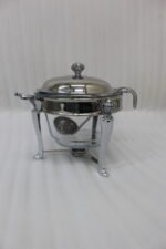 One More 4-liter glass chafing dish soup warmer with ornate stainless steel stand, ladle, and buffet burner on a wooden dining table.