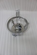 One More premium glass serving bowl set with an ornate silver-plated stand and two matching serving spoons placed on a dining table.