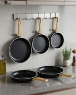 A collection of Turkish-made diamond-infused non-stick frying pans in various sizes ranging from 20cm to 30cm, displayed on a kitchen wall and countertop at OneMore.