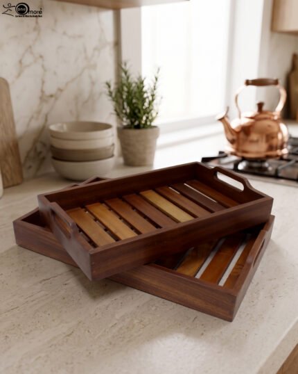 Two stacked, high-quality wooden serving trays resting on a kitchen countertop with a copper kettle and plant in the background.